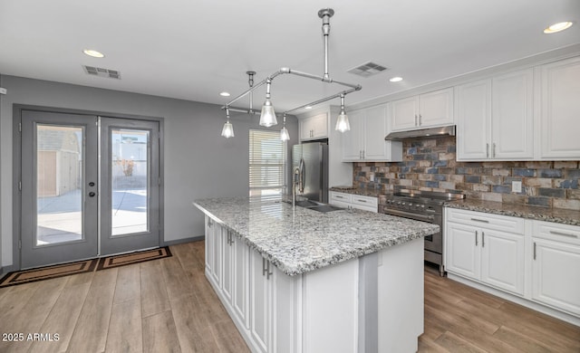 kitchen featuring pendant lighting, an island with sink, white cabinetry, decorative backsplash, and stainless steel appliances