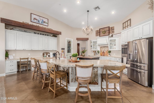 kitchen with a breakfast bar area, a kitchen island with sink, hanging light fixtures, white cabinetry, and stainless steel appliances