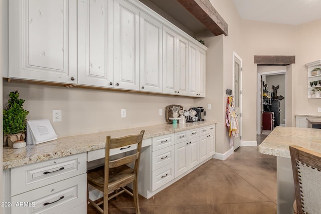 interior space with light stone counters, built in desk, and white cabinets