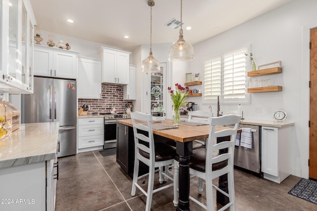 kitchen featuring appliances with stainless steel finishes, pendant lighting, tasteful backsplash, white cabinetry, and light stone counters