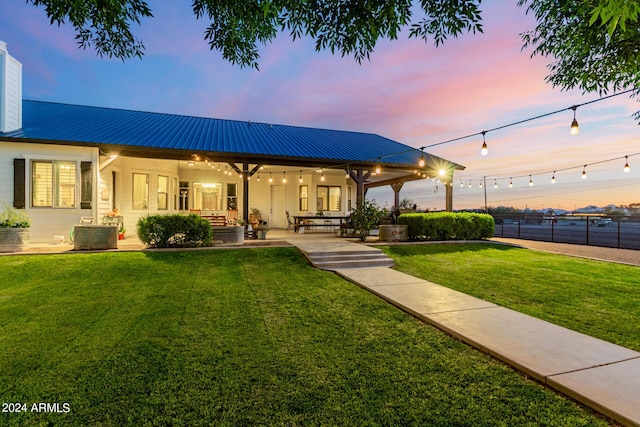 back house at dusk featuring a yard and a patio area