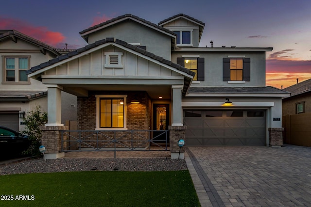 craftsman-style home with stucco siding, an attached garage, covered porch, decorative driveway, and brick siding