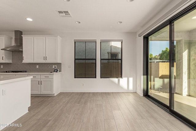 kitchen with visible vents, light wood-style floors, light countertops, wall chimney range hood, and white cabinetry