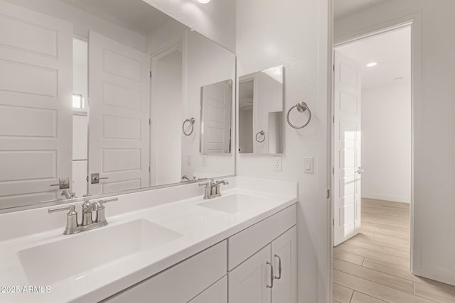 full bath with double vanity, wood finished floors, a sink, and baseboards