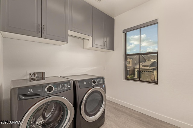 washroom featuring light wood-type flooring, washing machine and dryer, cabinet space, and baseboards