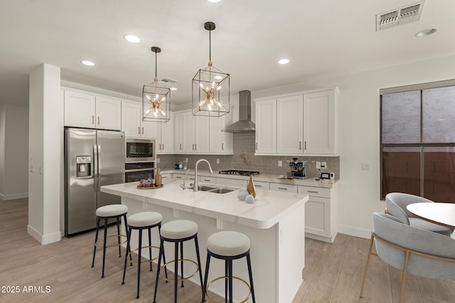 kitchen featuring stainless steel appliances, visible vents, backsplash, a sink, and wall chimney range hood