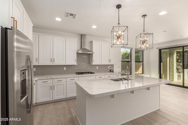 kitchen featuring a sink, visible vents, wall chimney range hood, light wood-type flooring, and stainless steel fridge with ice dispenser