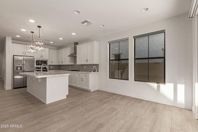 kitchen featuring light countertops, visible vents, appliances with stainless steel finishes, light wood-type flooring, and wall chimney exhaust hood