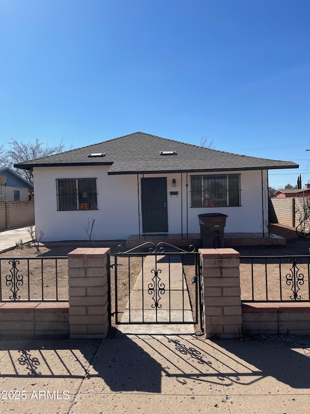 view of front facade featuring a fenced front yard, a gate, roof with shingles, and stucco siding