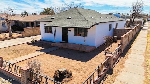 view of front facade with roof with shingles, fence, and stucco siding