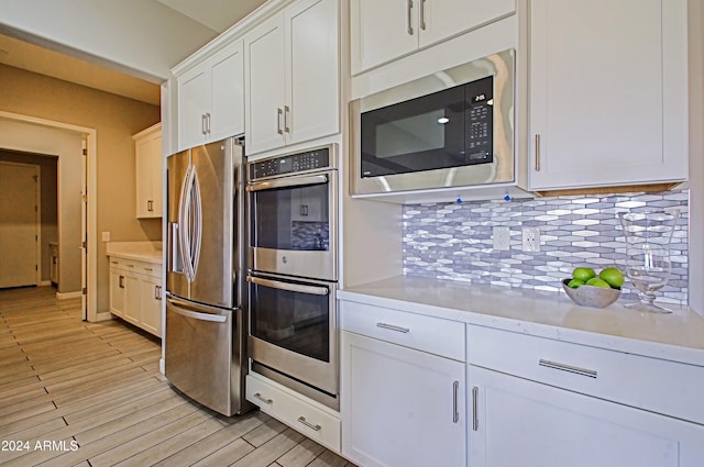 kitchen with backsplash, stainless steel appliances, light hardwood / wood-style flooring, and white cabinets