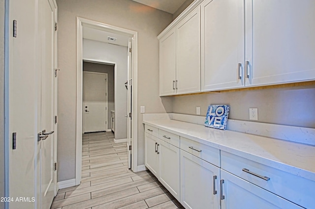 kitchen with white cabinetry, light stone countertops, and light wood-type flooring