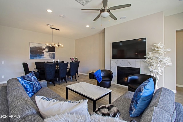 living room featuring light hardwood / wood-style flooring, ceiling fan with notable chandelier, and a fireplace