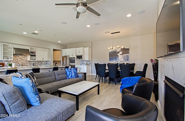 living room featuring light hardwood / wood-style floors, a premium fireplace, and ceiling fan with notable chandelier