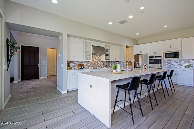 kitchen with appliances with stainless steel finishes, white cabinetry, wall chimney range hood, and a large island