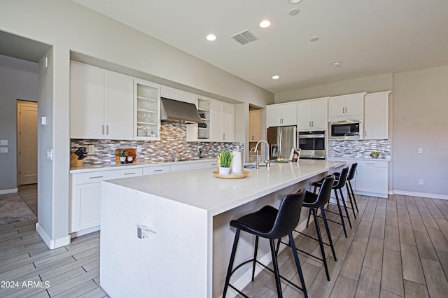 kitchen with a kitchen breakfast bar, white cabinetry, stainless steel appliances, extractor fan, and a center island with sink