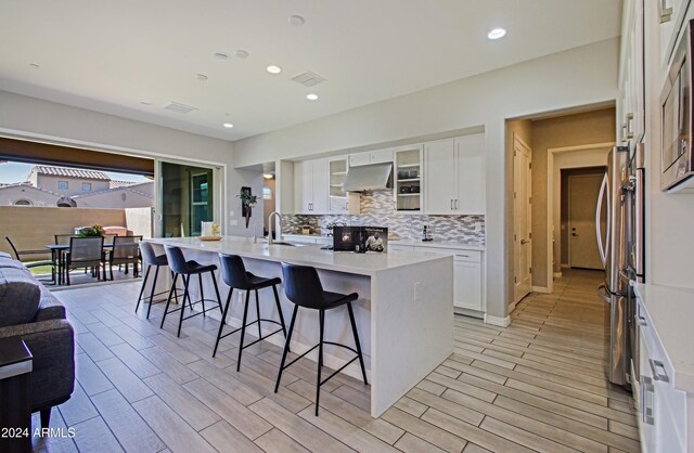 kitchen featuring light wood-type flooring, white cabinetry, range hood, a breakfast bar area, and a center island with sink