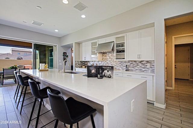 kitchen featuring range hood, light hardwood / wood-style flooring, white cabinetry, and a breakfast bar area