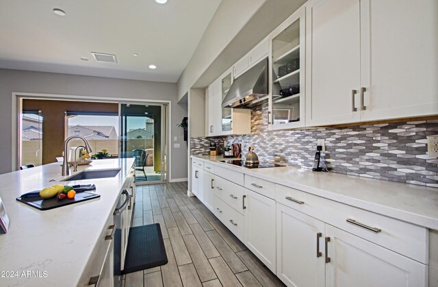 kitchen featuring sink, black electric cooktop, white cabinetry, range hood, and decorative backsplash