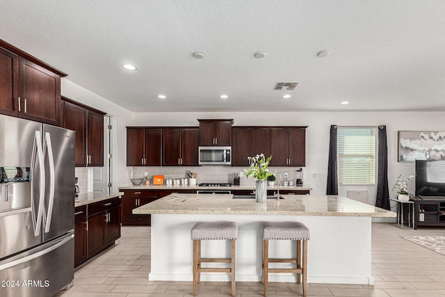 kitchen with a center island with sink, a breakfast bar, appliances with stainless steel finishes, light stone countertops, and light hardwood / wood-style flooring