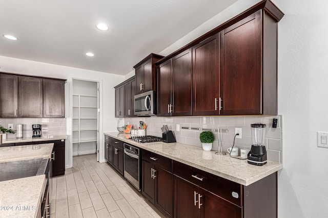 kitchen with light stone counters, decorative backsplash, appliances with stainless steel finishes, and light hardwood / wood-style flooring