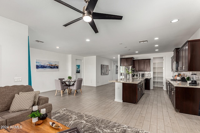 kitchen with light wood-type flooring, appliances with stainless steel finishes, dark brown cabinetry, decorative backsplash, and an island with sink