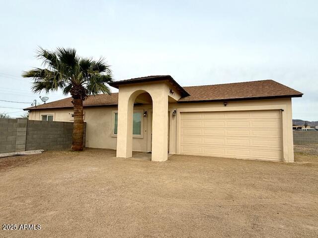 view of front facade with stucco siding, a garage, driveway, and fence