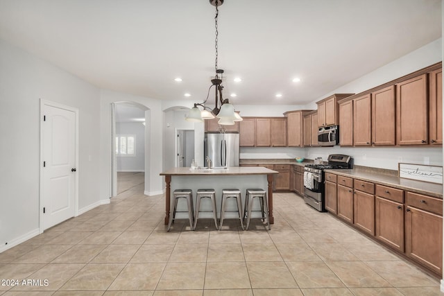 kitchen with light tile patterned floors, a breakfast bar area, stainless steel appliances, a center island, and decorative light fixtures