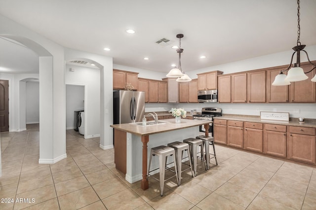 kitchen featuring pendant lighting, appliances with stainless steel finishes, a kitchen bar, and a kitchen island with sink