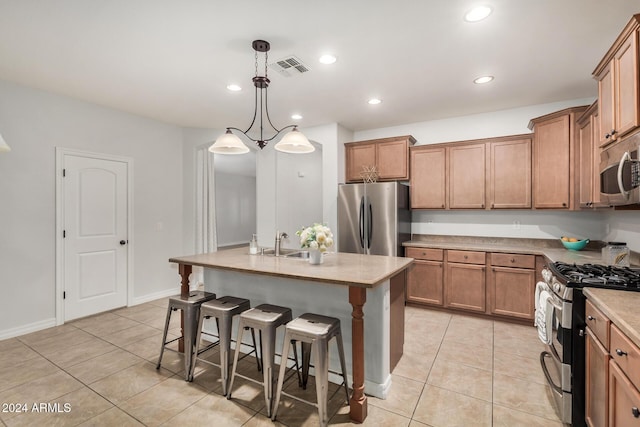 kitchen featuring appliances with stainless steel finishes, hanging light fixtures, a center island with sink, a kitchen bar, and light tile patterned flooring