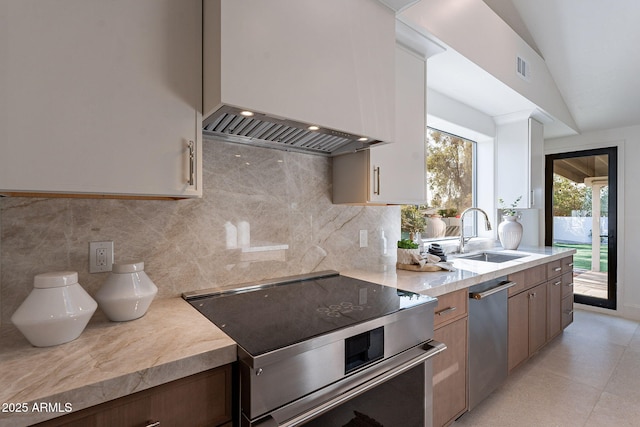 kitchen with vaulted ceiling, appliances with stainless steel finishes, sink, premium range hood, and tasteful backsplash