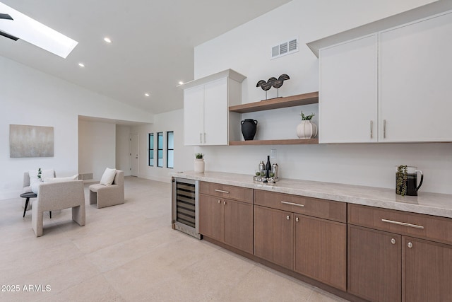 kitchen with white cabinets, light tile patterned floors, wine cooler, and vaulted ceiling with skylight