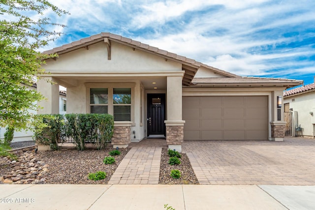 view of front of property featuring an attached garage, stone siding, decorative driveway, and stucco siding