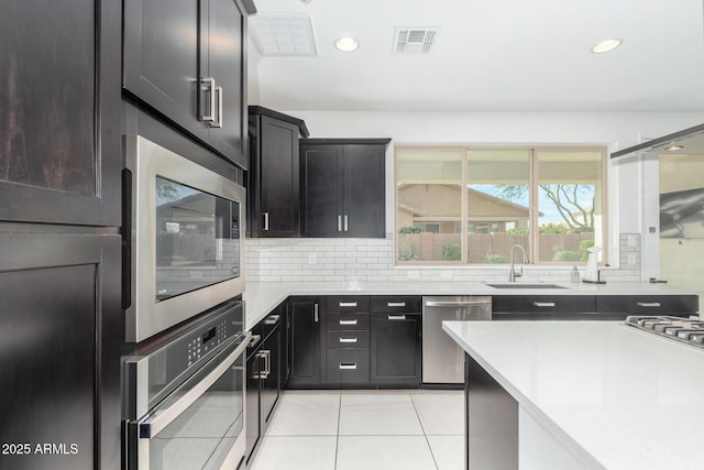 kitchen with appliances with stainless steel finishes, a sink, visible vents, and tasteful backsplash