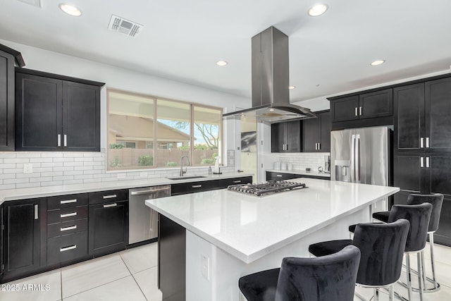 kitchen with visible vents, appliances with stainless steel finishes, dark cabinets, island exhaust hood, and a sink