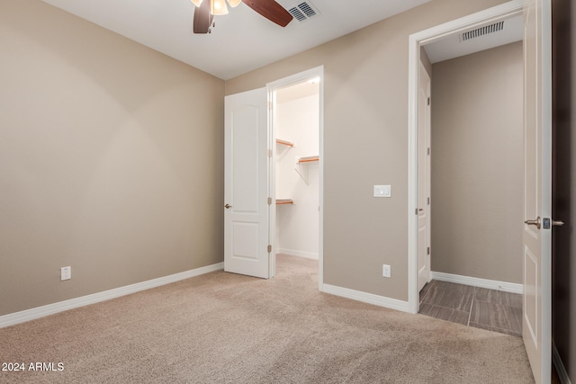 unfurnished bedroom with a walk in closet, ceiling fan, a closet, and light carpet