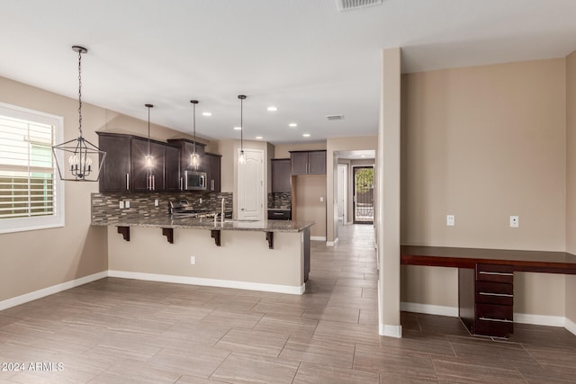 kitchen featuring dark brown cabinetry, stainless steel appliances, light stone counters, kitchen peninsula, and pendant lighting