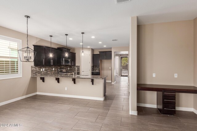 kitchen with light stone countertops, stainless steel appliances, tasteful backsplash, kitchen peninsula, and pendant lighting