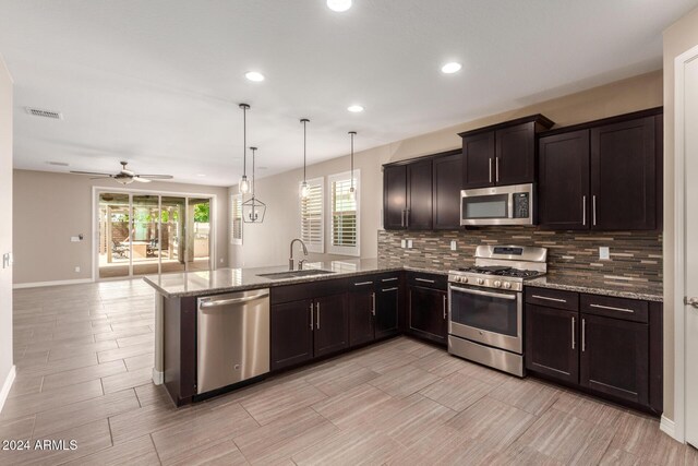 kitchen with light stone countertops, sink, hanging light fixtures, kitchen peninsula, and appliances with stainless steel finishes