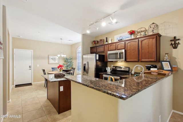 kitchen featuring dark stone counters, stainless steel appliances, decorative light fixtures, an inviting chandelier, and light tile patterned flooring