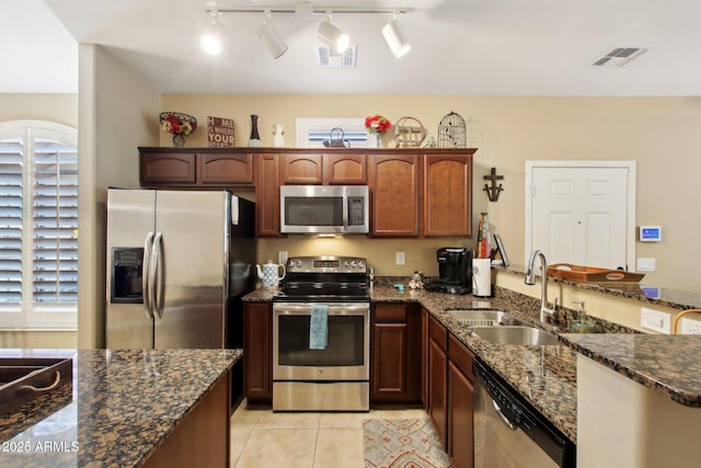 kitchen featuring kitchen peninsula, appliances with stainless steel finishes, sink, light tile patterned floors, and dark stone countertops