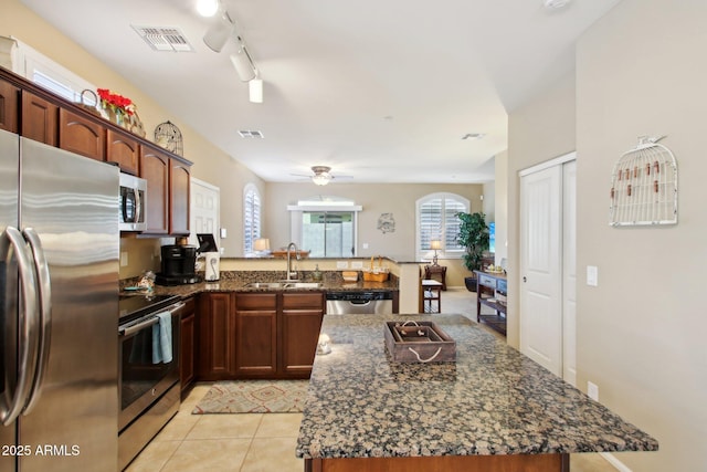 kitchen featuring ceiling fan, sink, dark stone counters, a kitchen island, and appliances with stainless steel finishes