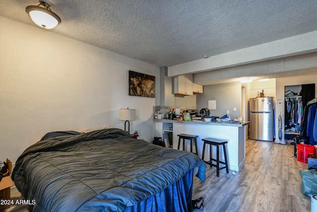 bedroom featuring light wood-type flooring, stainless steel fridge, a textured ceiling, and a closet