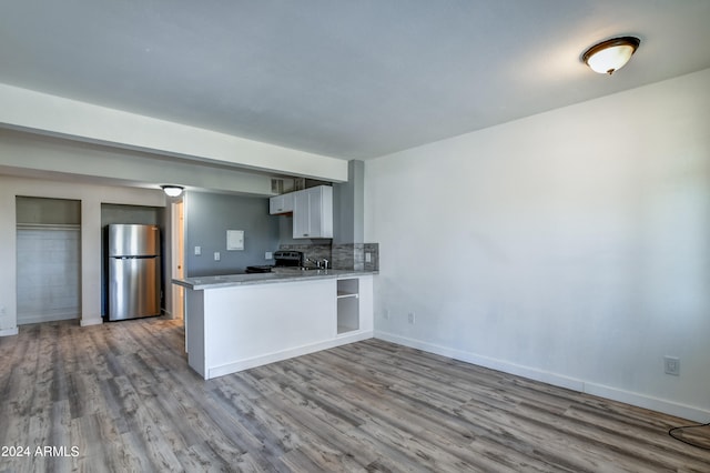 kitchen with backsplash, stainless steel refrigerator, hardwood / wood-style flooring, and kitchen peninsula