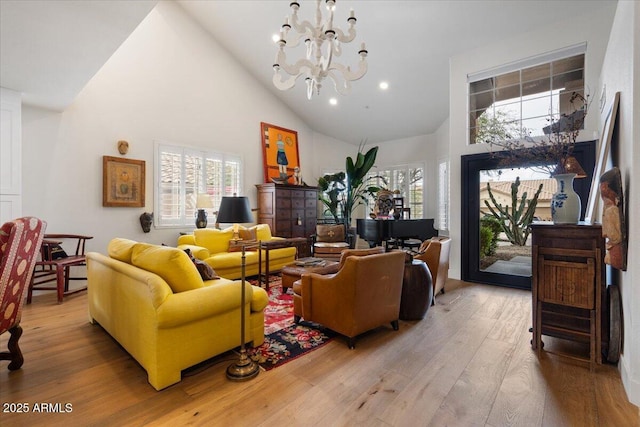 living room featuring a healthy amount of sunlight, high vaulted ceiling, light wood-type flooring, and a notable chandelier