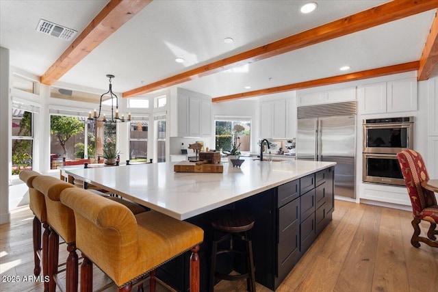 kitchen featuring decorative light fixtures, stainless steel appliances, white cabinetry, and a large island with sink