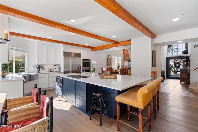 kitchen featuring a kitchen bar, a spacious island, beam ceiling, built in appliances, and white cabinets