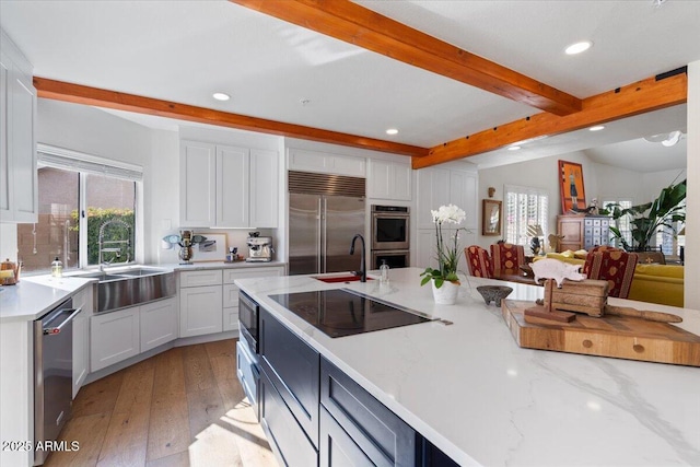 kitchen featuring light stone counters, sink, beam ceiling, built in appliances, and white cabinetry