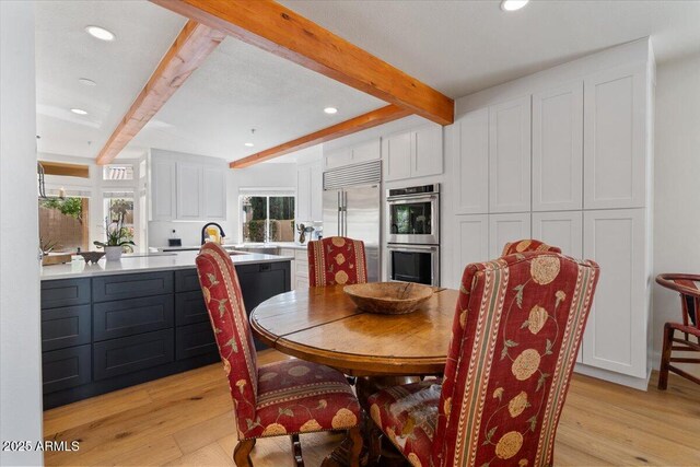 dining area featuring beam ceiling, light wood-type flooring, and sink