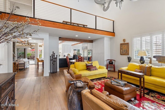 living room with beam ceiling, a towering ceiling, and light hardwood / wood-style flooring